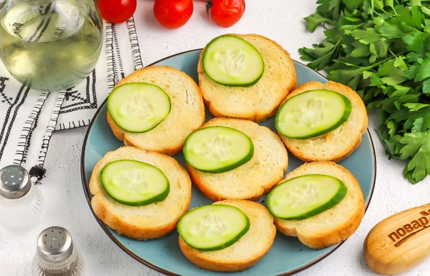 1. Этап. Брускетты в аэрогриле: В это время промойте огурец и нарежьте его кружочками, промойте зеленый лук. Выложите ломтики огурца на поджаренные тосты.