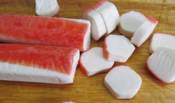 1. Этап. Сырный суп с крабовыми палочками: Крабовые палочки достаньте из морозилки, чтобы они оттаяли, если вы используете замороженный продукт. Затем нарежьте их на кружочки толщиной менее одного сантиметра. Выложите крабовые палочки в суп, перемешайте.