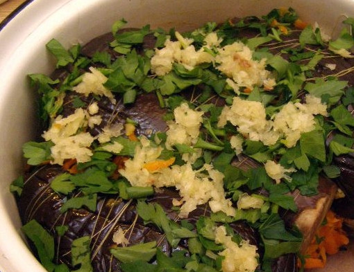 1. Этап. Синенькие с морковкой на зиму: Выложите овощи в кастрюлю, присыпьте их отложенной зеленью и чесноком.