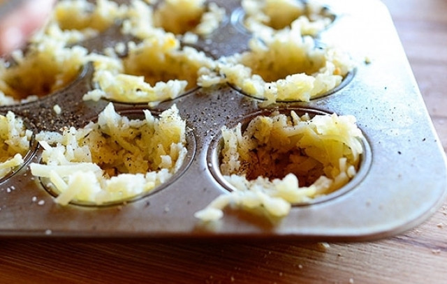 1. Этап. Картофельная яичница: Возьмите формочки для маффинов и смажьте их растительным маслом. Затем выложите в каждую емкость по паре столовых ложек тертого запеченного картофеля и сформируйте из него корзинки. Присыпьте их солью и перцем.