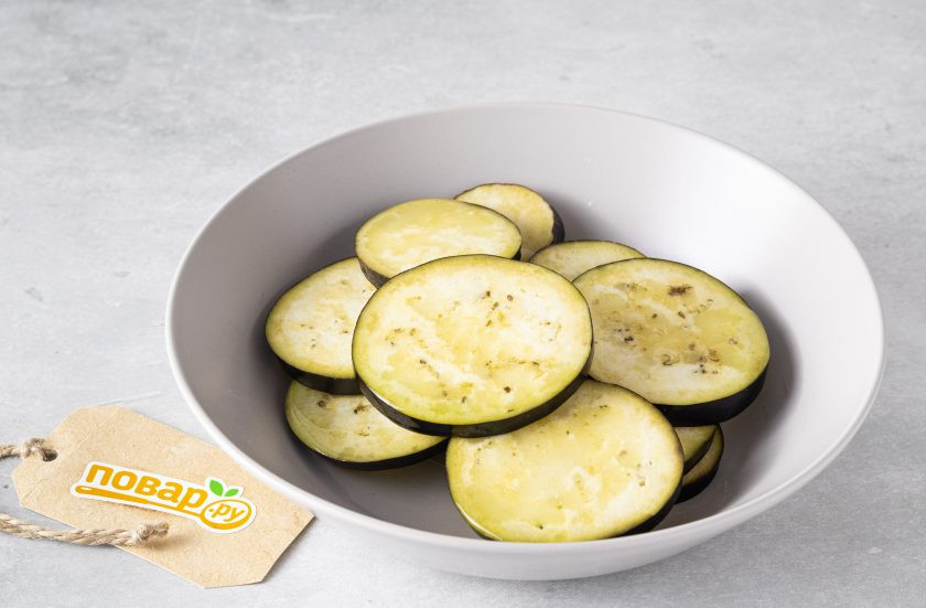 1. Этап. Салат с баклажанами и вялеными помидорами: Баклажан помойте, нарежьте кружочками толщиной 0,5 см. Добавьте растительное масло и все перемешайте, чтобы кружочки равномерно пропитались маслом.