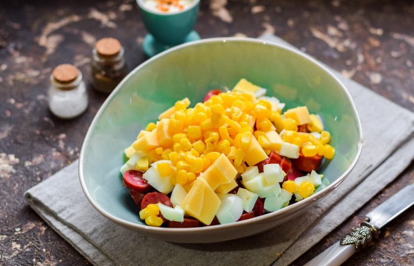 1. Этап. Салат Ежик с колбасой: Добавьте следом в салат консервированную кукурузу.