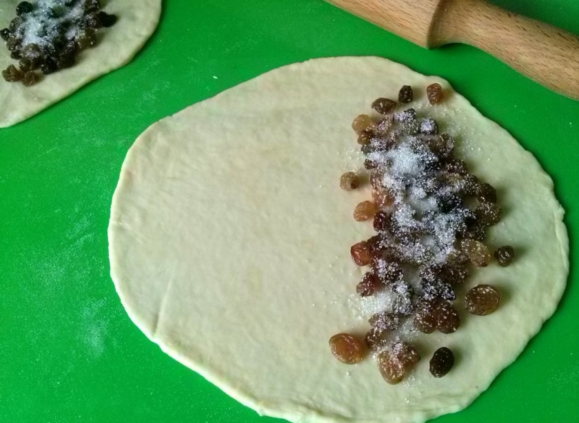 1. Этап. Ляваш: 6. Спустя 40 минут делим наше тесто приблизительно на 12 шариков размеров с куриное яйцо, каждый из которых раскатываем примерно до размера сковороды, в которой будем жарить. Сковорода должна быть достаточно большой, поскольку ляваш по размерам соотносим с чебуреками. На одну половину раскатанного теста выкладываем часть изюма, присыпаем его сахаром.