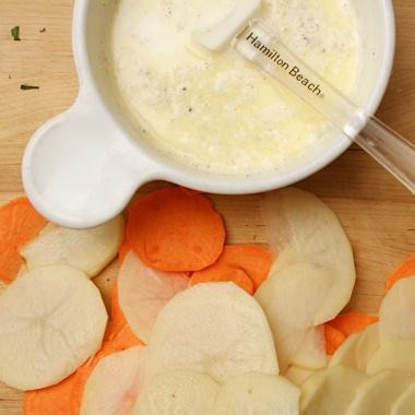 1. Этап. Картофельная запеканка с сырным соусом: 1. Очистить картофель и нарезать ломтиками толщиной около 8 мм. Измельчить чеснок. Натереть сыр Грюйер на крупной терке. Разогреть духовку до 200 градусов. В небольшой кастрюле смешать жирные сливки, молоко, сливочное масло и чеснок, довести на слабом огне. Снять соус с огня.