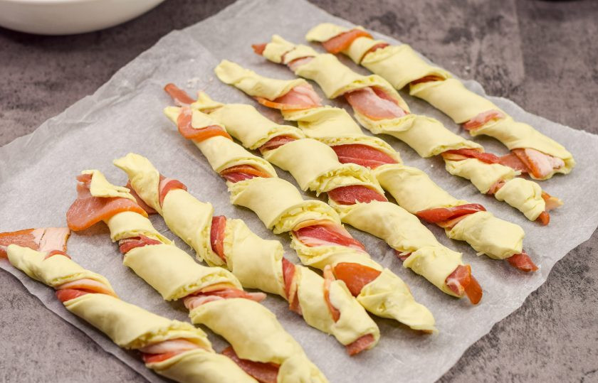 1. Этап. Слоеные палочки с сыром и беконом: Скрутите каждую полоску заготовки, чтобы бекон был внутри. Духовку разогрейте до 180 градусов.