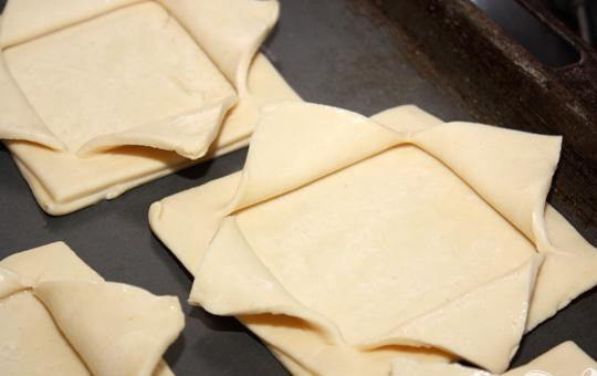 1. Этап. Тарталетки из слоеного теста: 4. Теперь на приготовленный противень раскладываем целые квадраты и каждый из них смазываем яйцом. Затем на все целые квадраты кладем сверху по одному надрезанному квадрату. В том случае если у Вас крестообразные надрезы, то надо отгибать уголки наружу. Должны получиться лепесточки.