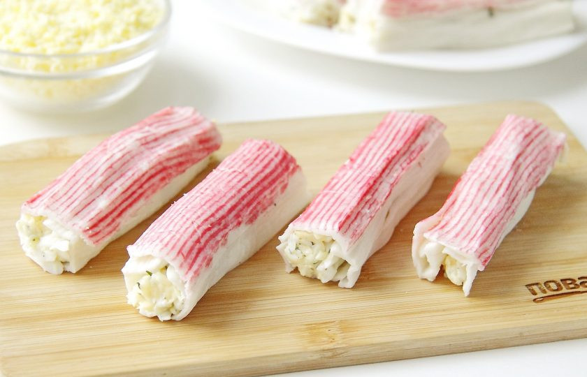 1. Этап. Новогодние рулетики из крабовых палочек: Аккуратно сверните палочку в трубочку, чтобы начинка оказалась внутри. Таким образом наполните все крабовые палочки.