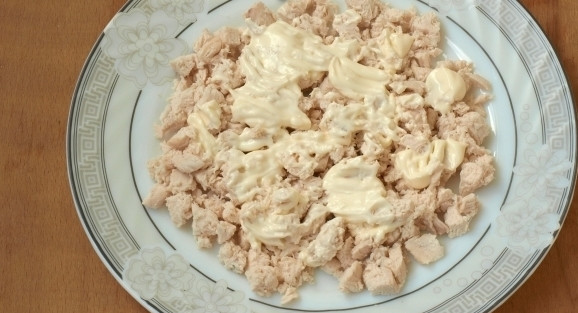 1. Этап. Слоеный салат с корейской морковью: Нарежьте кусочками куриное филе, уложите его первым слоем в салатницу. Промажьте его заправкой.