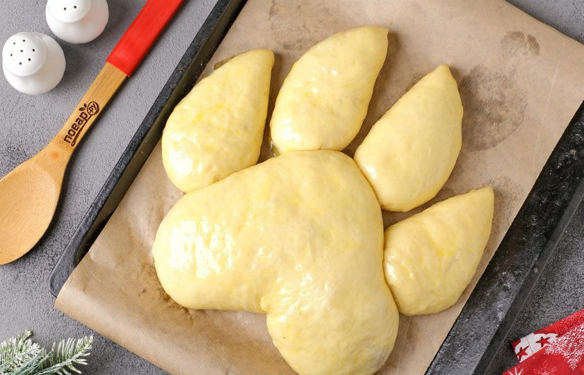1. Этап. Мясной пирог Лапа тигра: А теперь самое ответственное задание! Необходимо выложить заготовки швом вниз на застеленный пергаментом противень в форме следа лапы тигра. Большую часть кладем первой и руками придаём ей нужную форму. Тесто очень пластичное и с ним невероятно легко работать. Заготовки поменьше выложите сверху, руками придайте нужный изгиб. Накройте тесто полотенцем и дайте постоять 20 минут, затем смажьте желтком (можно разбавить чуть-чуть молоком). Запекайте в духовке при температуре 180 градусов около 40 минут. Верх должен подрумяниться.