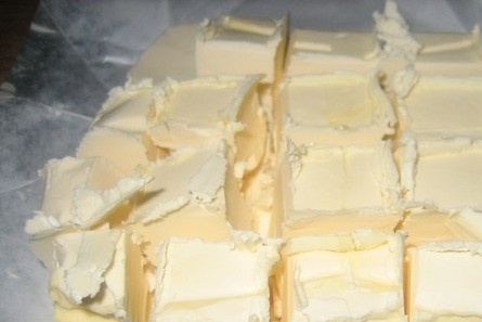 1. Этап. Торт на сковороде с творогом: Из холодильника достаньте сливочное масло. Дайте ему постоять, чтобы оно стало мягким. Затем разрежьте его на кубики и добавьте в горячее молоко.