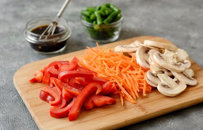 1. Этап. Гречневая лапша вок с овощами: Болгарский перец помойте, удалите семена и хвостик. Нарежьте соломкой. Шампиньоны нарежьте пластинами. Стручковую фасоль разморозьте. Морковь очистите от кожуры и нарежьте на терке для корейской моркови.