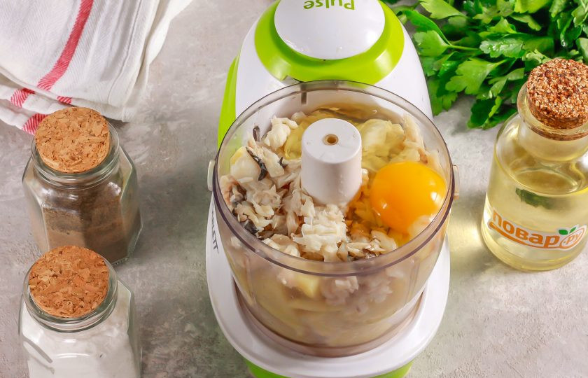 1. Этап. Рыбная запеканка как в детском саду: Отварной хек разберите в руках, удаляя косточки и кожу. Очищенную мякоть выложите в чашу измельчителя вместе с отварным картофелем, вбейте куриное яйцо. Всыпьте соль и молотый черный перец.