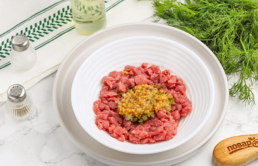 1. Этап. Тартар из говядины классический: Добавьте измельченные каперсы и дижонскую (зерновую) горчицу. Каперсы можно заменить солеными корнишонами или огурцами. При нарезке продуктов из рассола нужно оставить нарезку на доске 5 минут, чтобы из нее слилась лишняя жидкость.