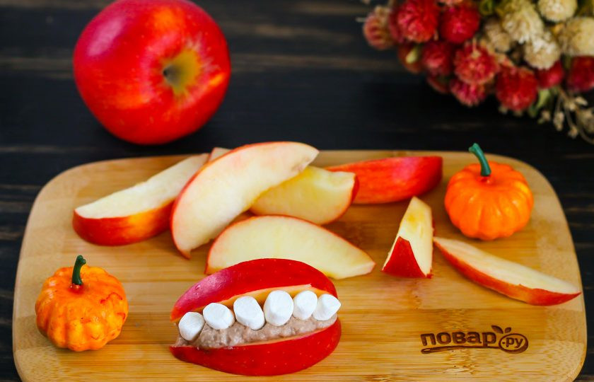 1. Этап. Улыбка с зубами на Хэллоуин: Яблоки промойте, разрежьте на четыре части, удалите семенные блоки. Нарежьте крупными дольками. На одну дольку выложите часть крема и вставьте в него 6-7 зубов. Посередине зубки должны быть крупными, по бокам - мелкими, как у людей. Если маршмеллоу длинные, нарежьте их ножницами пополам. Накройте вторым ломтиком яблока, чтобы получилась устрашающая улыбка.