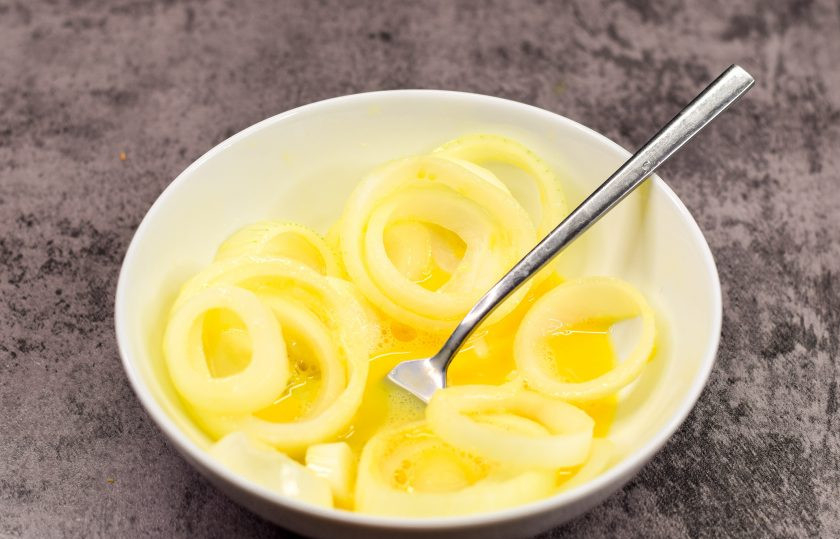 1. Этап. Обжаренные луковые кольца: В отдельной миске соедините куриное яйцо и две ложки воды, взболтайте немного и переложите сюда кольца лука.