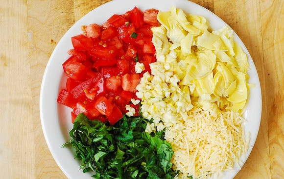 1. Этап. Куриное филе под шубой в духовке: 2. За это время вымойте, обсушите и измельчите помидор, артишоки, чеснок и зелень. Твердый сыр натрите на терке.