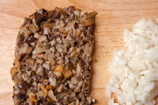 1. Этап. Запеканка с солеными грибами: 2. Параллельно промойте, обсушите и измельчите грибочки. Лук очистите и нарежьте мелкими кубиками. Вымойте и измельчите зелень.