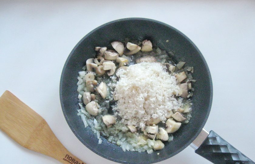 1. Этап. Ризотто с креветками и грибами: Всыпьте в сковороду рис, который предварительно помойте, стараясь сильно не вымывать крахмал. На слабом огне перемешивая, поджарьте рис в течение 1 минуты.