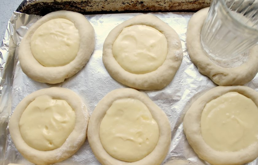 1. Этап. Ватрушки с маскарпоне: Подошедшее тесто разделите на одинаковые части и скатайте шарики. Противень смажьте растительным маслом и разложите шарики из теста на расстоянии, накройте и дайте постоять 15 минут. За это время тесто увеличится в размерах. Сделайте углубления в шариках и разложите начинку. Яйцо перемешайте до однородности и смажьте тесто.