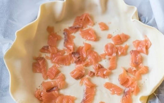 1. Этап. Закусочный пирог со шпинатом и семгой: 4. Готовое слоеное тесто раскатайте в пласт на листе пергамента и перенесите прямо на бумаге в форму для выпечки (диаметром 25 см) или в глубокую сковороду. Наколите тесто вилкой и разложите кусочки копченой семги.