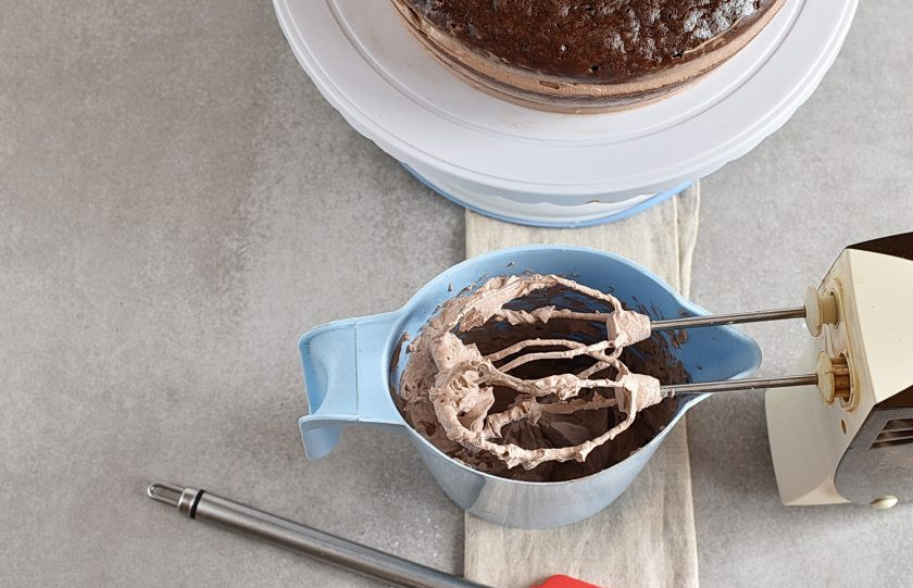 1. Этап. Торт в мультиварке: Взбейте холодные сливки с тремя столовыми ложками сахарной пудры и остатками какао в пышный крем. Выложите третий корж и покройте торт взбитыми сливками сверху и с боков.