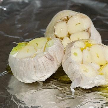 1. Этап. Суп с запеченным чесноком, помидорами и сыром: 4. Обрезать 3 головки чеснока, добавить 2 столовые ложки оливкового масла. Плотно завернуть головки в фольгу, положить рядом с помидорами и запекать в течение 40 минут. Как только помидоры и чеснок будут готовы, остудить их немного. Отжать чесночную мякоть в миску и выбросить кожицу.