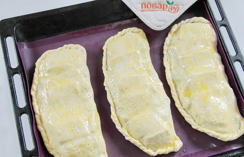 1. Этап. Кальцоне с цукини, оливками и моцареллой: Приготовьте аналогично другие кальцоне и выложите их на противень, застеленный пергаментом или силиконовым ковриком. Смажьте кальцоне взбитым желтком и сделайте проколы вилкой для выхода пара.