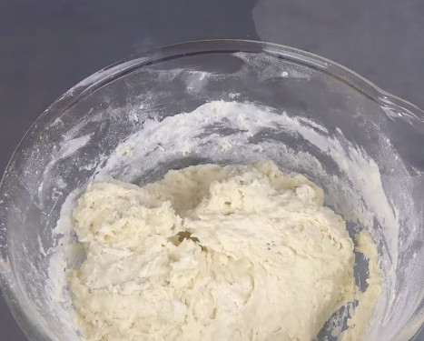 1. Этап. Хлеб на сковороде: 2. Также по центру влейте растительное масло, выложите сметану и добавьте соду. Начните замешивать тесто из центра, понемногу доливая кефир. В конце просейте ещё немного муки и перемешайте руками. Тесто должно быть липким и мягким.