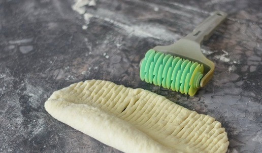 1. Этап. Сдобный калач на сливках: Скатайте пласт теста в тугой рулет, оставив небольшой хвостик. Этот хвостик надрежьте ножом или роликом для теста и сверните рулет до конца.