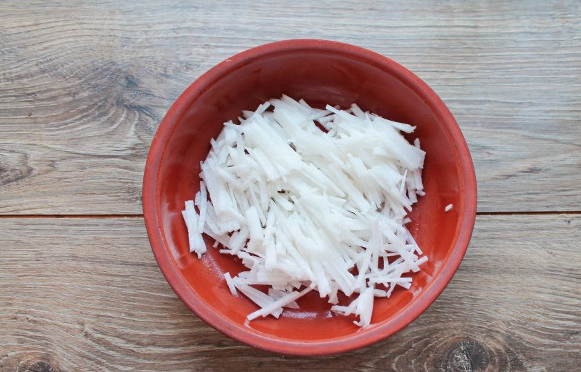 1. Этап. Салат с дайконом, огурцом и помидором: Дайкон почистите от кожуры и порежьте тонкой соломкой. Выложите дайкон в салатник.