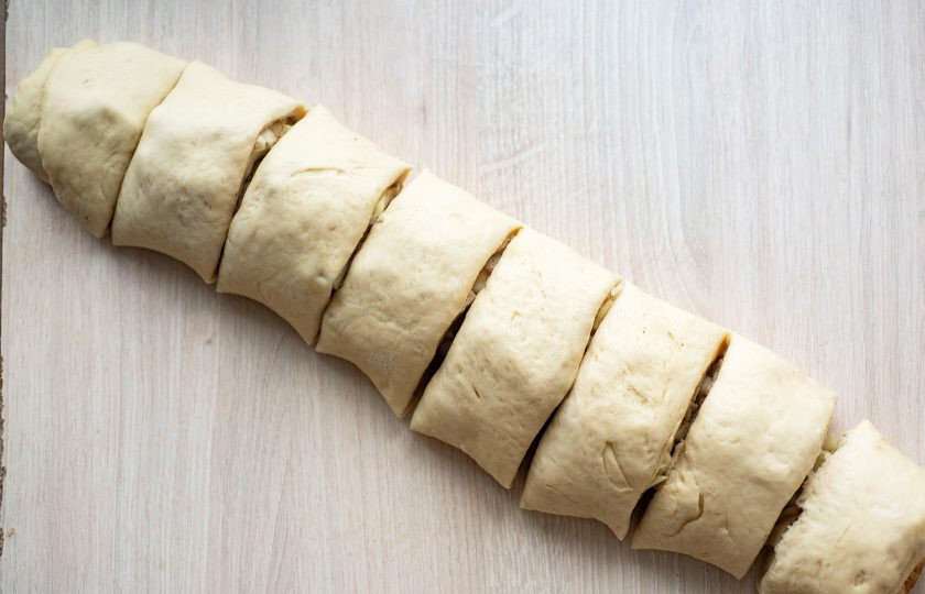 1. Этап. Булочки с яблоком и корицей из дрожжевого теста: Сверните тесто с начинкой рулетом и нарежьте на одинаковые части.