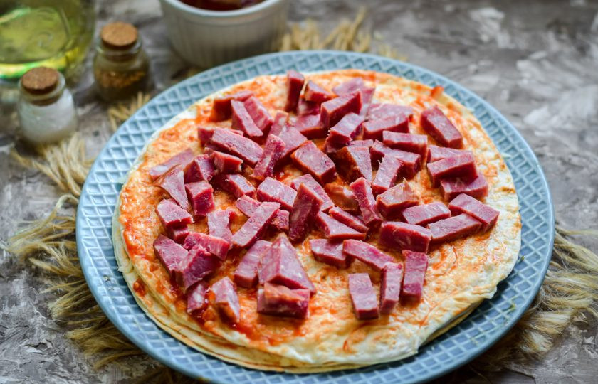 1. Этап. Пицца на сковороде за 15 минут: Теперь смажьте лаваш соусом. Колбасу нарежьте средними кусками и разложите поверх лаваша.