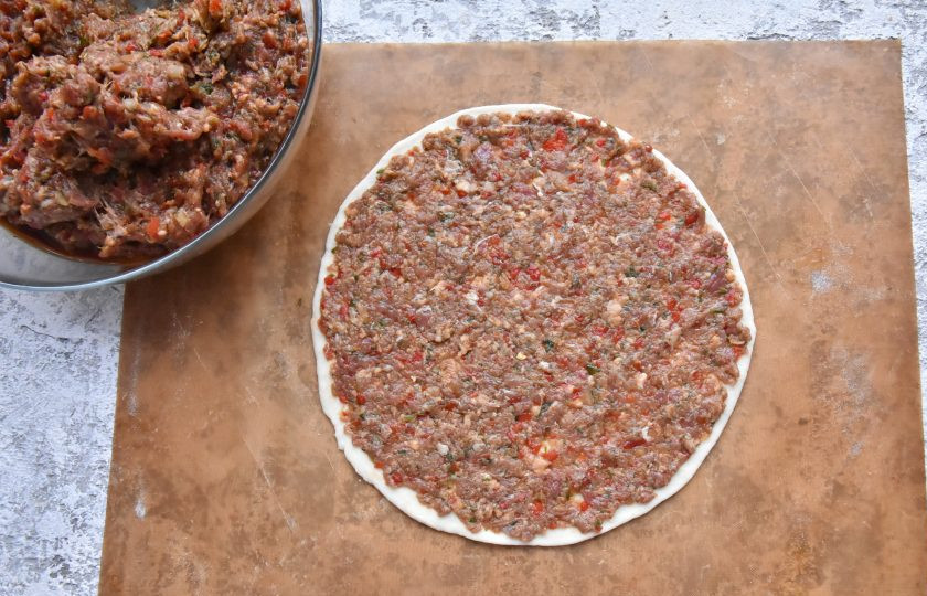 1. Этап. Лахмаджун по-турецки: В центр лепешки выложите часть начинки из фарша и овощей (150-200 граммов) и распределите ее равномерным, тонким слоем по всей поверхности теста.