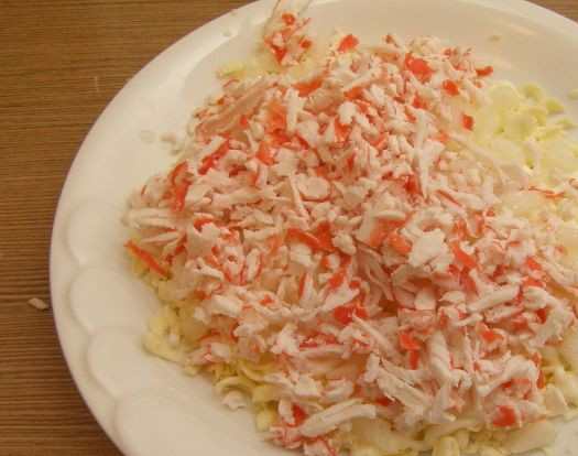 1. Этап. Крабовый салат с плавленым сыром: Лук у нас уже замариновался, сливаем маринад. Выкладываем лук на слой сыра, а поверх него - четвертую часть натертых крабовых палочек. Смазываем майонезом.