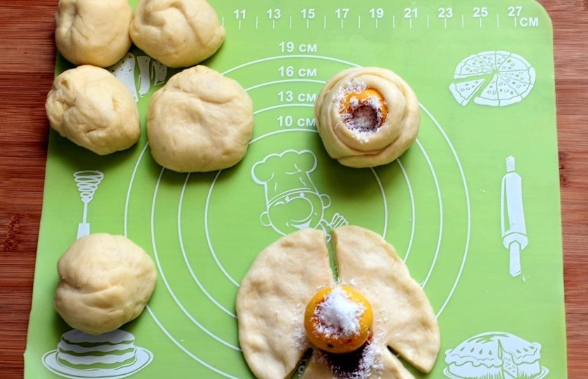 1. Этап. Сдобные розочки с ранетками: Раскатайте шарик теста в кружок и сделайте по краям три надреза, не доходя до центра. На середину уложите ранетку, налейте в отверстие немного карамели или вареной сгущенки и посыпьте кокосовой стружкой. Потяните вверх один сектор и оберните вокруг ранетки. Затем последовательно заверните оставшиеся два, формируя круглую розочку.