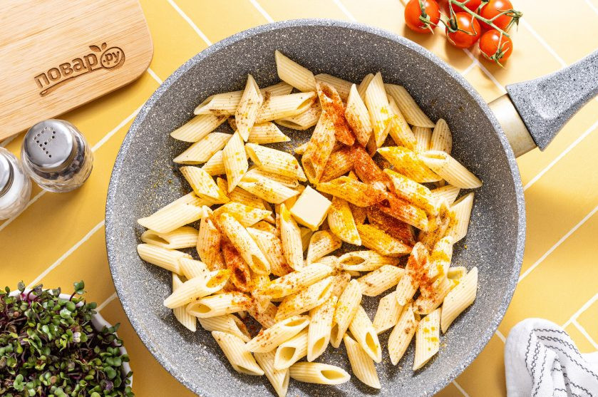 1. Этап. Макароны с куркумой: Выложите макароны в разогретую сковороду, добавьте сливочное масло, куркуму, молотый черный перец и копченую паприку.