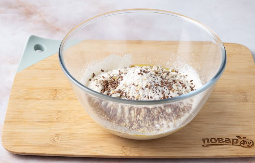 1. Этап. Зерновой хлеб на дрожжах: Затем просейте около половины муки и добавьте семечки. Все перемешайте и добавьте оставшуюся часть муки.