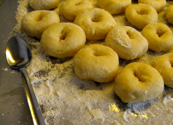 1. Этап. Тесто на пончики: Когда тесто хорошенько поднимется, начинаем отщипывать от него кусочки для будущих пончиков. Размер рассчитывайте на свое усмотрение. Не забудьте присыпать стол мукой, чтобы тесто не прилипало. Делаем из кусочков бублики с маленькой дырочкой. Оставляем пончики подняться минут на 10-15.