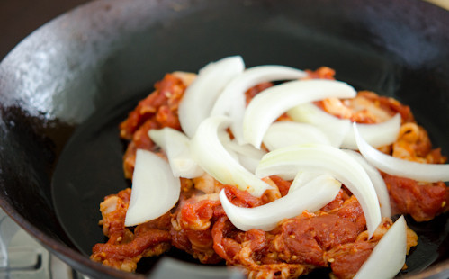 1. Этап. Свинина по-корейски: 5. На сковороду налить немного растительного масла (можно взять любое, которое есть под рукой). Отправить туда мясо, а сверху выложить лук. Перемешать и готовить на среднем огне, пока мясо не станет мягким.