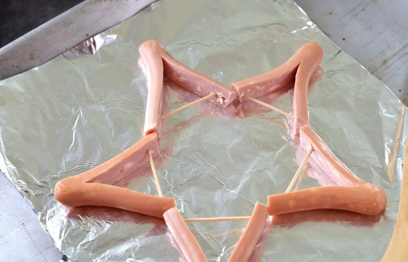 1. Этап. Звезды из сосисок и картофельного пюре: Выстелите противень фольгой, выложите на нее сосиски в виде звезды.