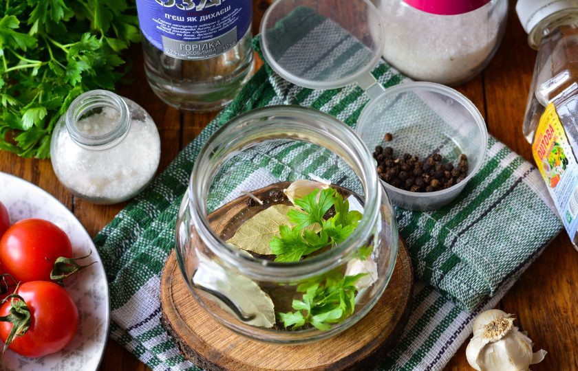 1. Этап. Помидоры с водкой на зиму: Выложите на дно простерилизованной банки специи: петрушку, чеснок, лавровый лист и перец горошком.