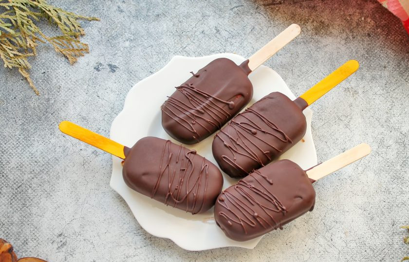 1. Этап. Творожное мороженое: Горький шоколад мелко поломайте и выложите в высокий стакан, в который без труда войдет мороженое. Влейте в шоколад масло и растопите в микроволновой печи в импульсном режиме, перемешивая, до однородности. Каждое мороженое окуните в шоколад, отстучите по краю стакана, чтобы убрать лишний шоколад и выложите на поднос, застеленный пленкой. Шоколад быстро застынет, поэтому украшайте мороженое сразу. Уберите в холодильник на 10 минут и подавайте к столу.