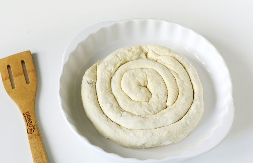 1. Этап. Слоеный пирог с мясом и грибами: Смажьте форму растительным маслом и выложите в нее рулеты из теста по кругу.