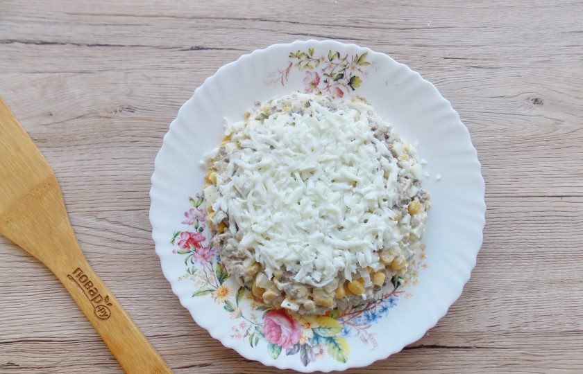 1. Этап. Салат Желтый одуванчик с кукурузой: Переложите салат на тарелку, формируя небольшую горку. Сверху выложите слоем натёртый на терке яичный белок. Бока обсыпьте натёртым яичным желтком. При помощи зелени (петрушки и укропа) выложите одуванчики.