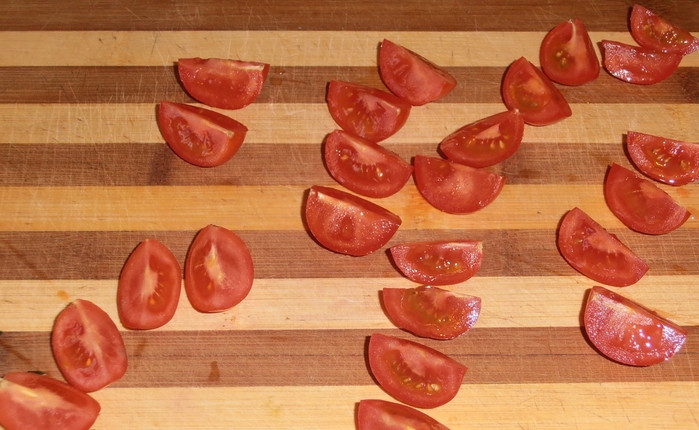 1. Этап. Новогодний салат из кальмаров: Помидоры черри промойте и разрежьте на половинки.