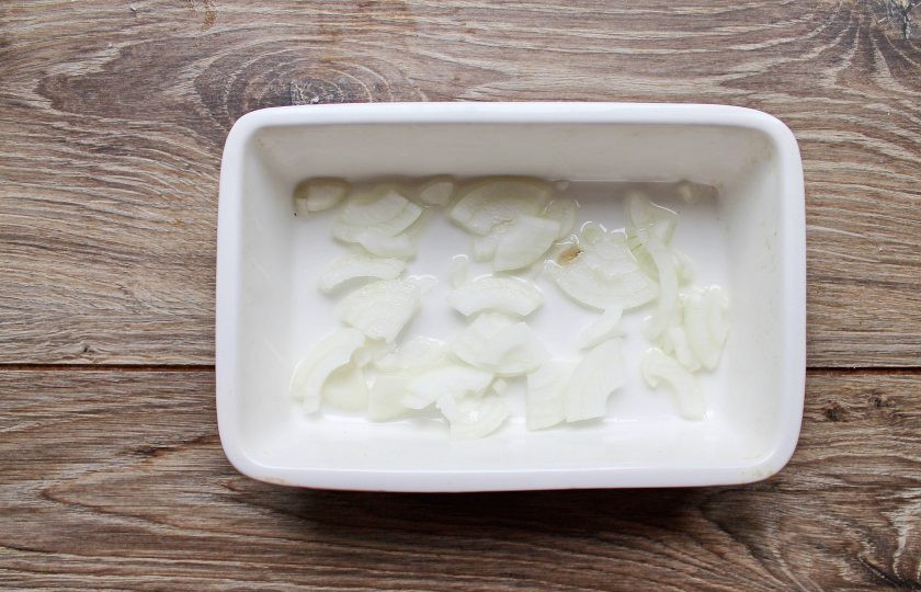 1. Этап. Навага жареная со сметанным соусом: Лук и чеснок мелко порежьте и выложите на дно формы.