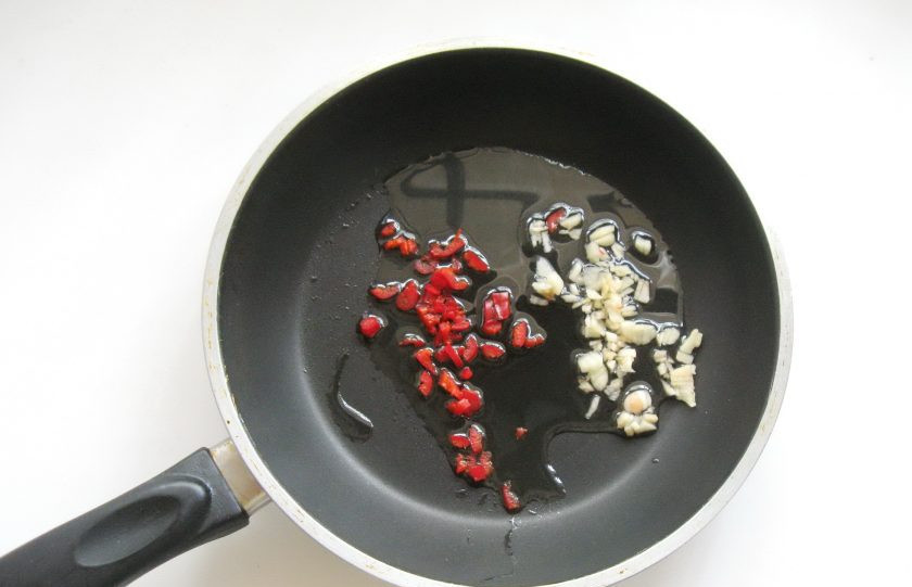1. Этап. Острая закуска из баклажанов: Красный жгучий перец, чеснок помойте и мелко нарежьте. Выложите в сковороду с подсолнечным маслом.