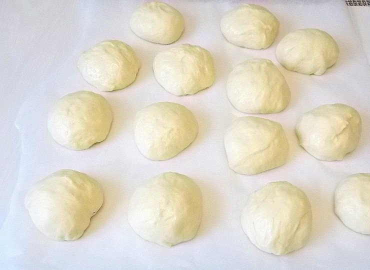 1. Этап. Советские пончики: Переложите тесто на стол и разделите его на одинаковые кусочки. Скатайте в шарики, выложите на бумагу для выпечки. Покройте полиэтиленом и оставьте для подъема еще на 20 минут.