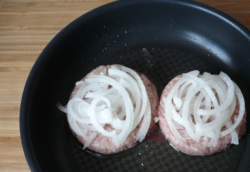 1. Этап. Двойной чизбургер Чили с жареным луком: Положите горсть нарезанного лука сверху на каждую котлету (на 2 котлеты понадобится примерно четверть лука) и расплющьте котлеты до толщины 0,5 см, вдавливая лук в каждую котлету. Жарьте, пока они не подрумянятся снизу, около 3 минут. Затем осторожно переверните котлеты вместе с луком и жарьте, пока лук не подрумянится и не станет мягким, ещё около 2 минут.