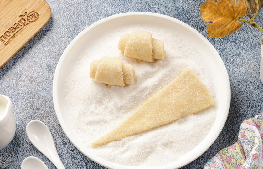 1. Этап. Пальчики дрожжевые: Каждый кусочек обваляйте с двух сторон в сахаре и сформируйте рогалик, начиная от широкой части по направлению к узкой.